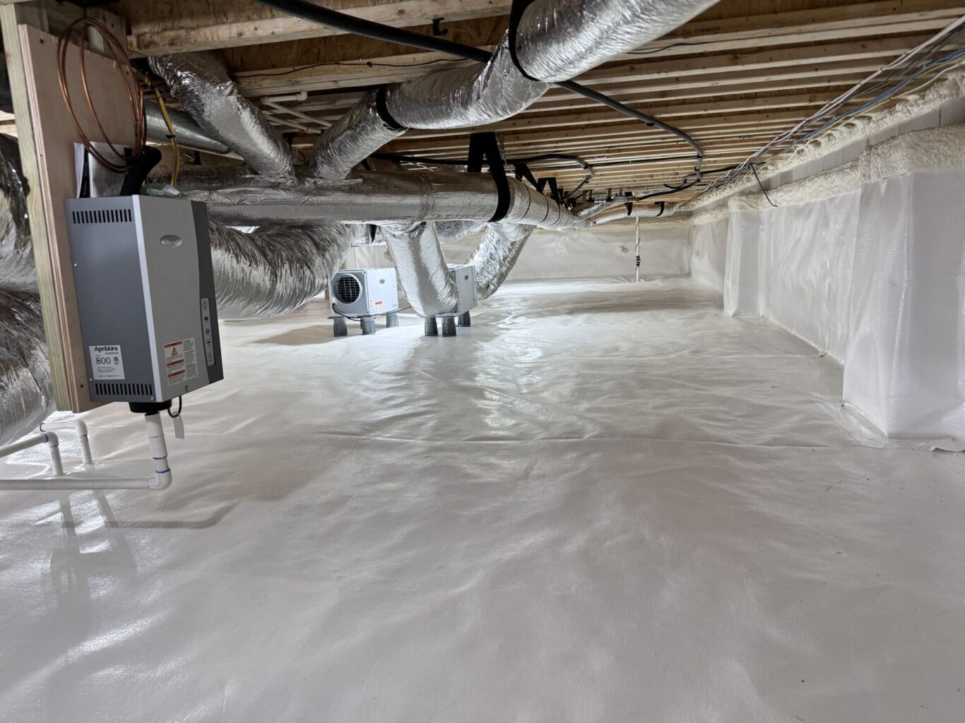 A clean, encapsulated crawl space with white vapor barrier on the floor and walls, exposed ductwork, and HVAC equipment installed overhead.