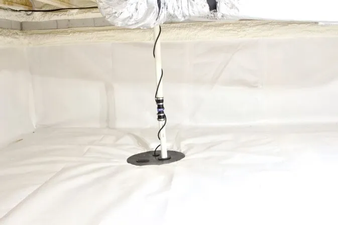 A sump pump discharge pipe extends through a circular opening in the white vapor barrier of a clean, encapsulated crawl space.