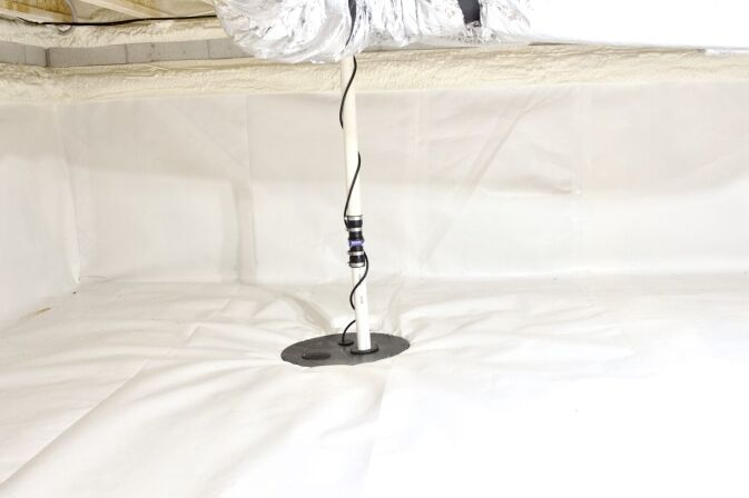 A sump pump discharge pipe extends through a circular opening in the white vapor barrier of a clean, encapsulated crawl space.