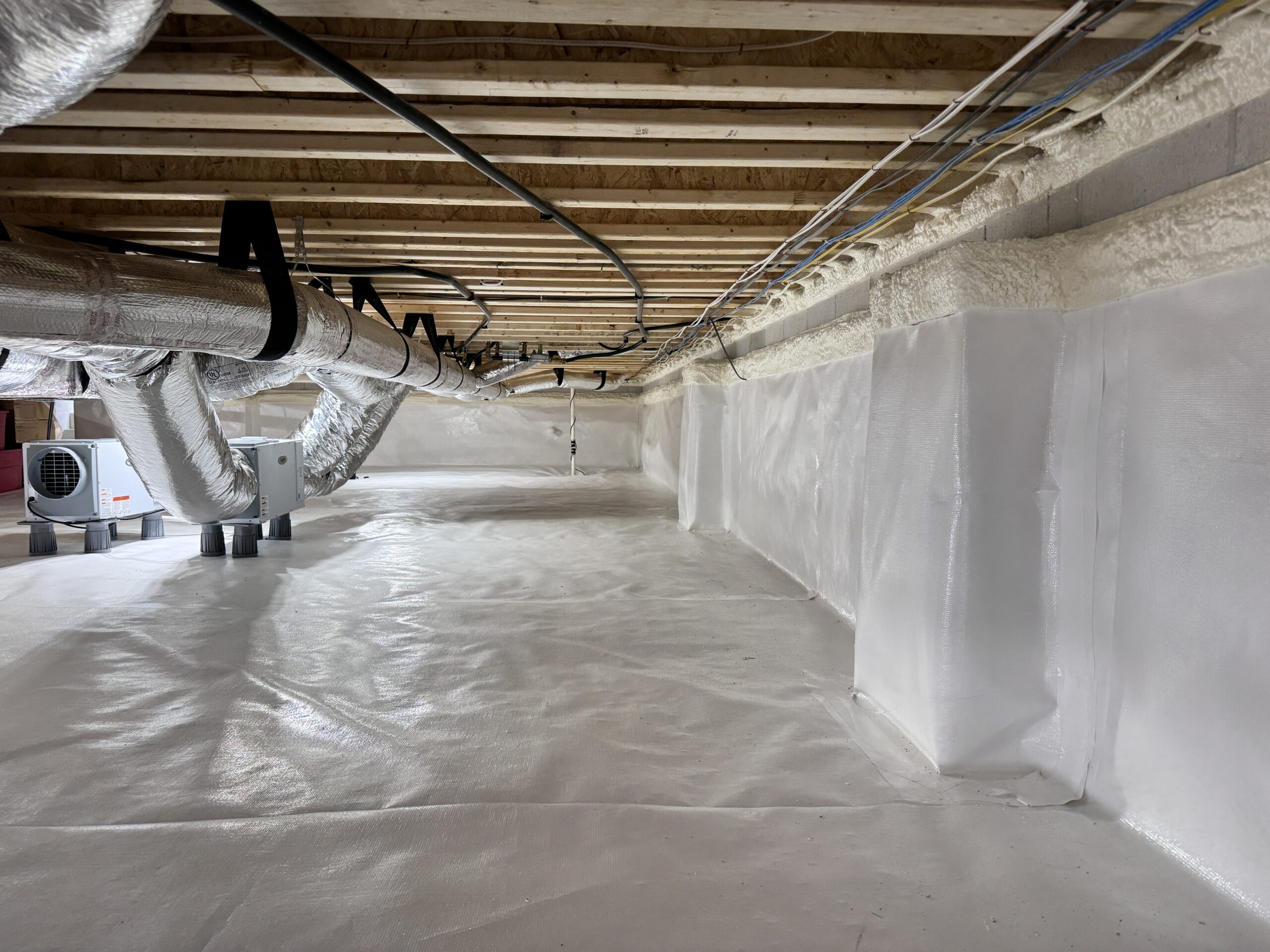 A clean, encapsulated crawl space with white plastic sheeting covering the floor and walls, exposed ceiling beams, and HVAC ducts running along the ceiling.