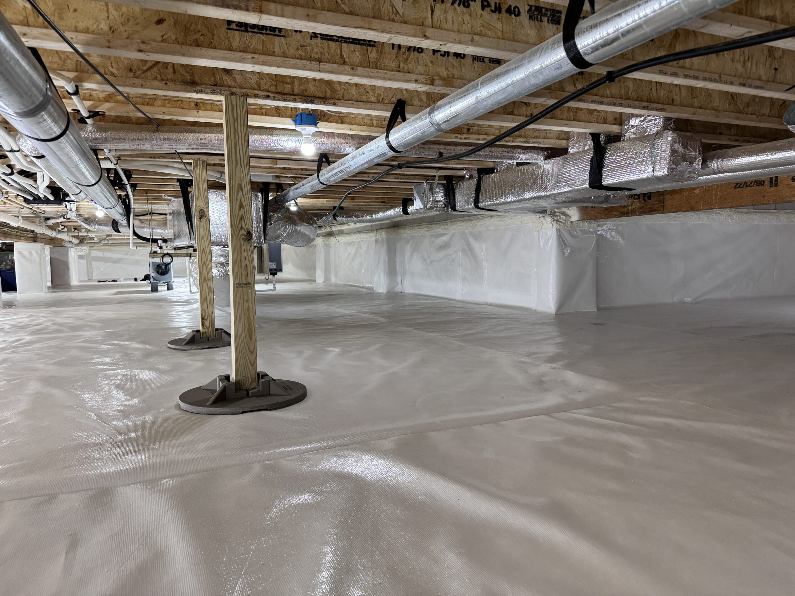 A clean, encapsulated crawl space with plastic sheeting on the floor and walls, exposed wooden beams above, and insulated HVAC ducts running along the ceiling.