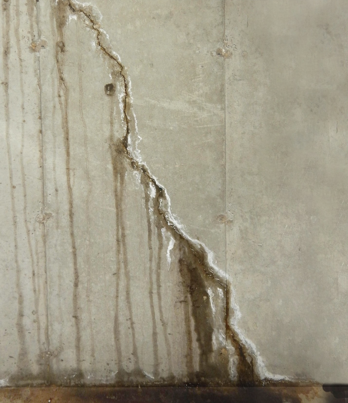 A concrete wall with a visible crack and brown water stains running down from the damaged area, indicating possible water leakage or seepage that may require professional waterproofing service.