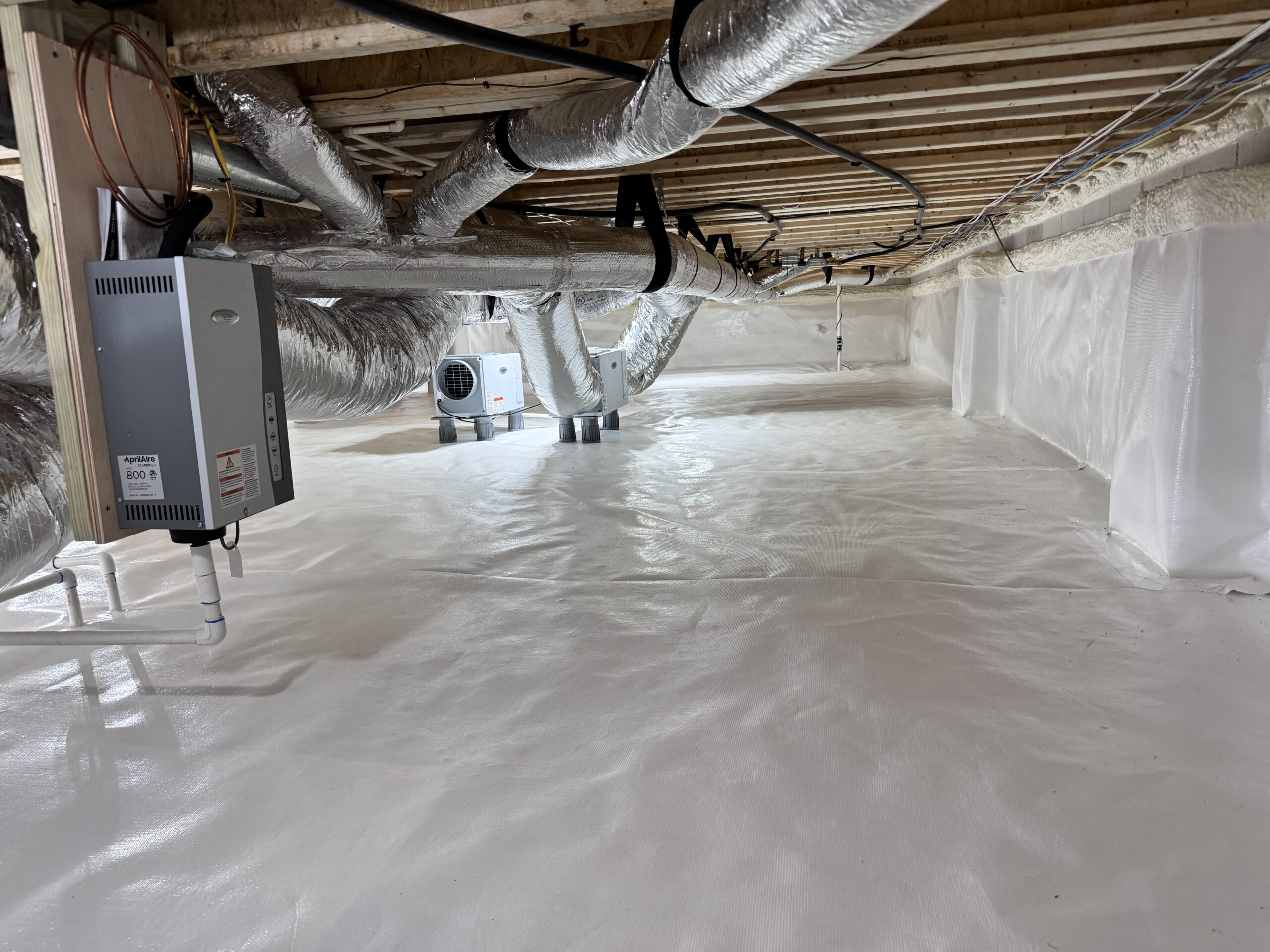 A clean, encapsulated crawl space with white vapor barrier on the floor and walls, exposed ductwork, and HVAC equipment installed overhead.